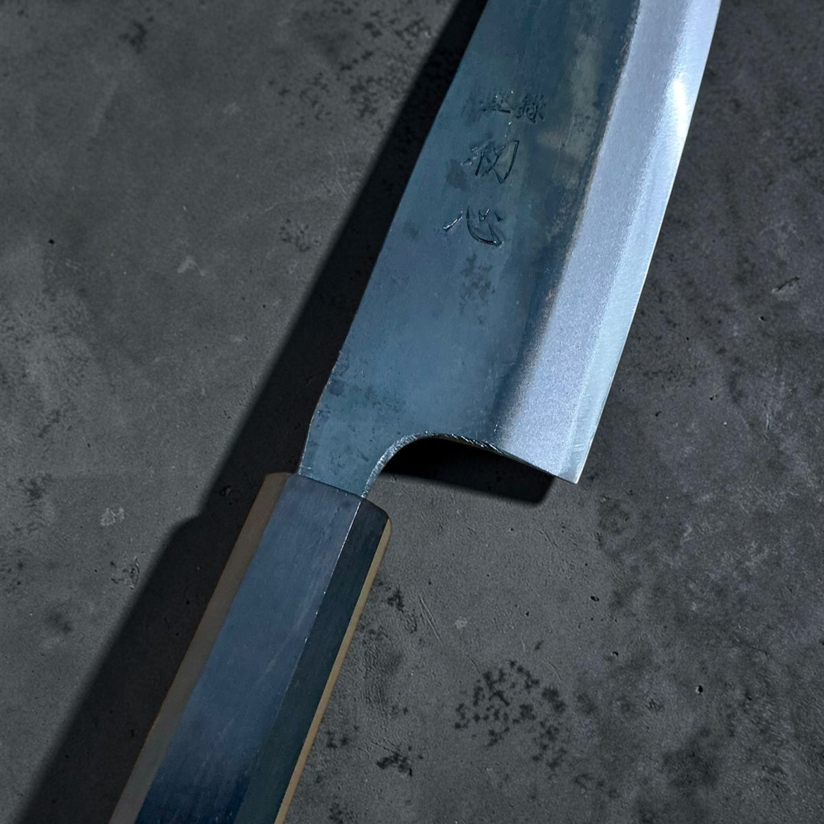 Close-up of the Hatsukokoro Kokugei Santoku heel, kanji, blade road, and mono ebony wa handle.