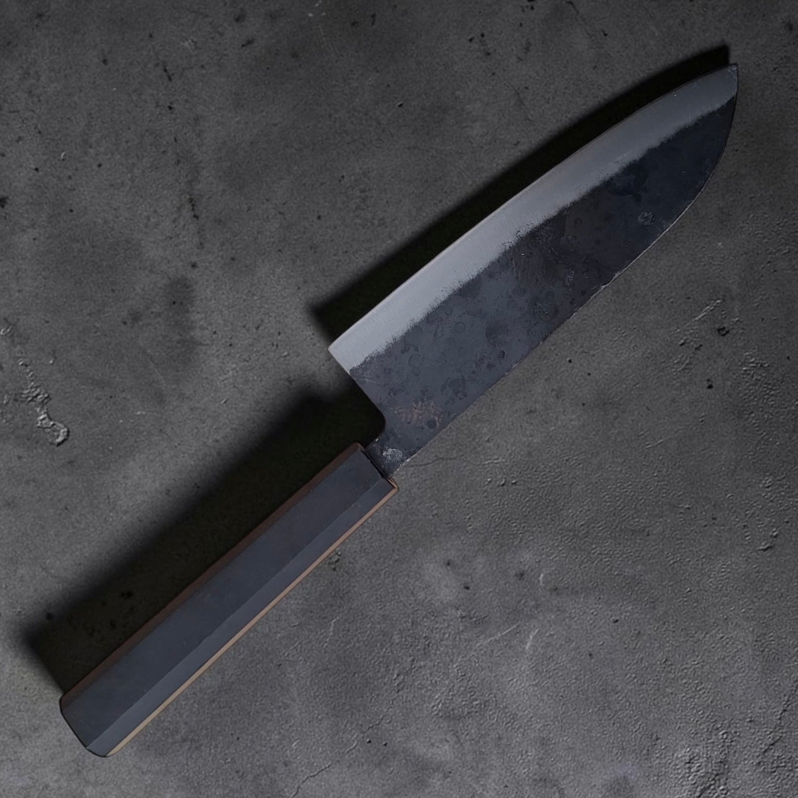 Angewinkelte Ansicht des Hatsukokoro Kurogane kurouchi Santoku mit Ebenholzgriff