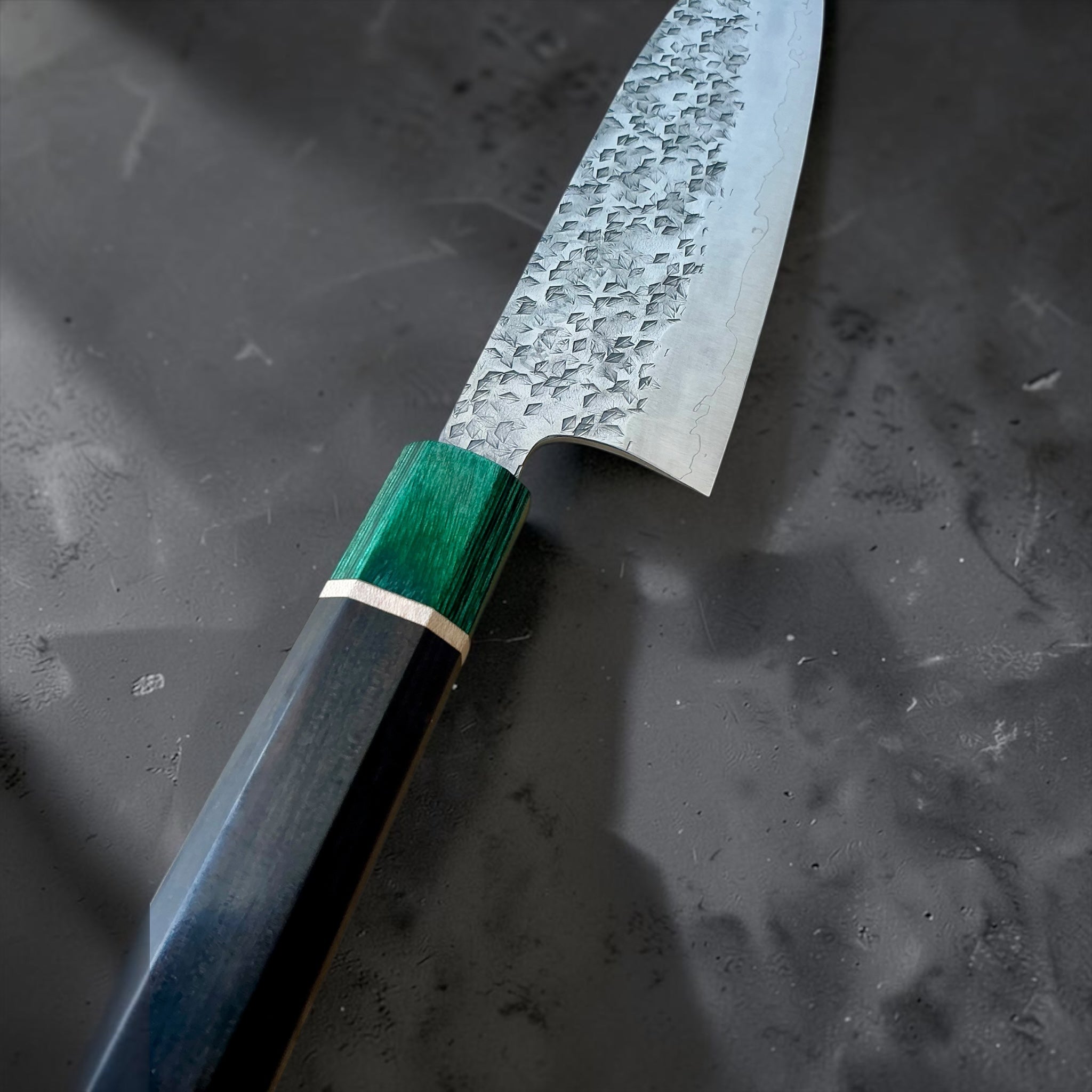 Nahaufnahme der gehämmerten Klinge des Makoto Kurosaki santoku, der grünen Zwinge und des hellen Griff-Zwischenrings
