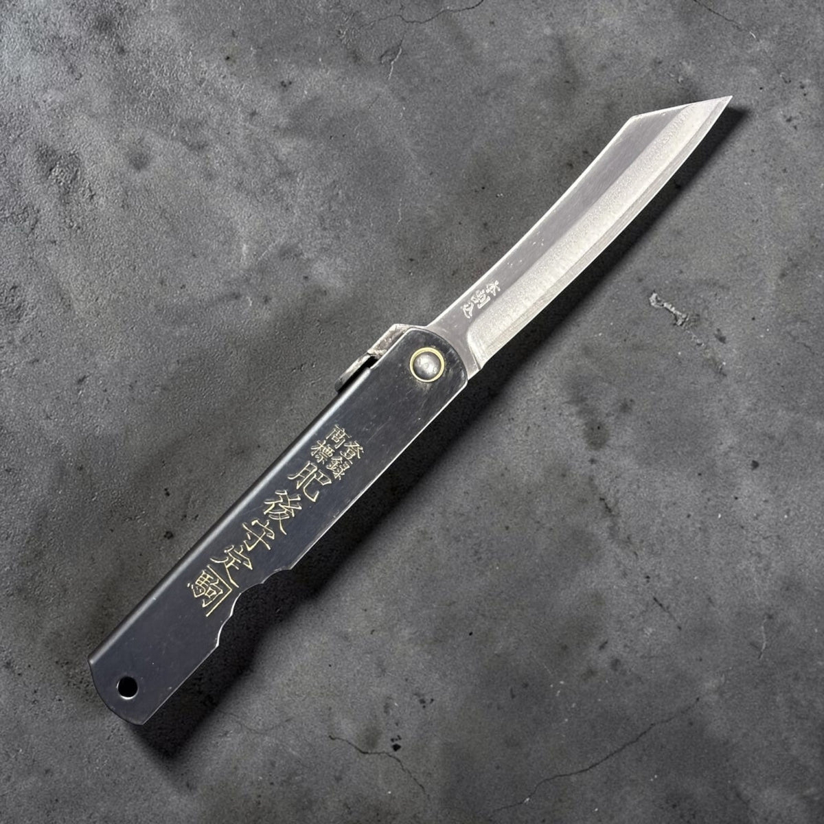 Nagao Higonokami SK carbon steel medium friction folder fully open, showing curved SK carbon blade and engraved black handle on neutral grey backdrop. #size_medium - black