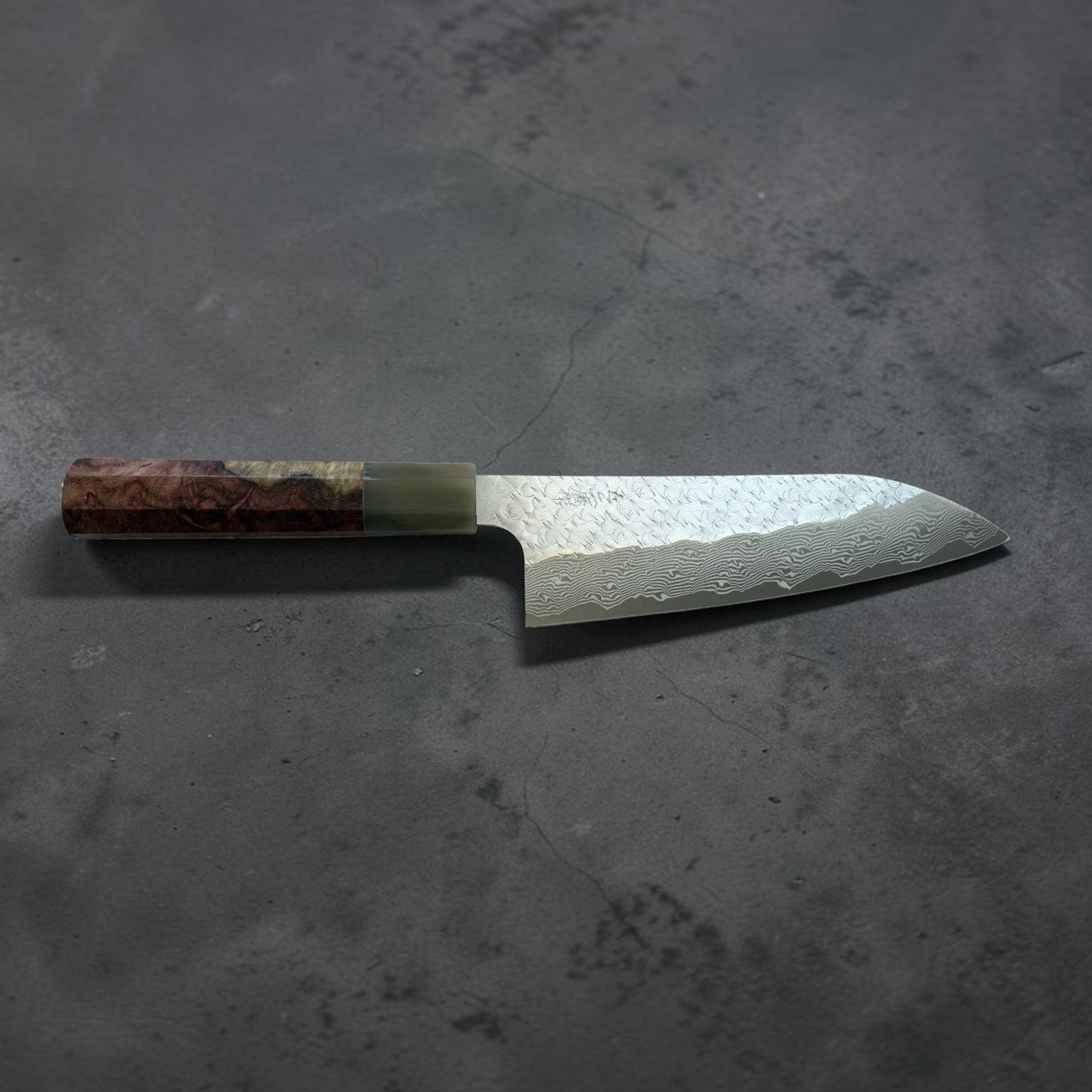 Nigara SG-STRIX Tsuchime Damascus Santoku 165 mm, horizontal profile view on dark textured background.