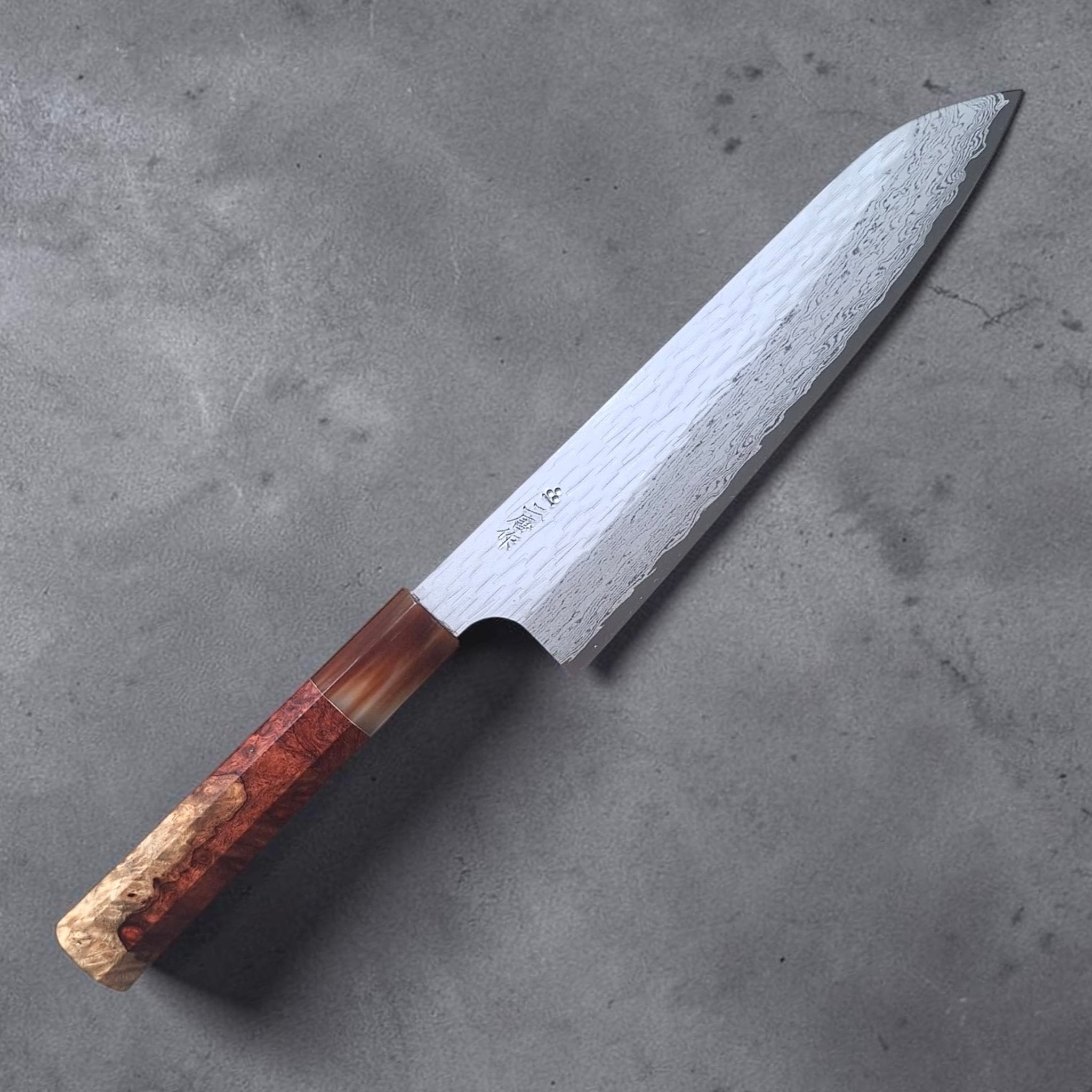 Nigara VG XEOS Tsuchime Gyuto 210 mm with amboyna burl and horn handle, angled full-knife product photo on a grey textured surface.
