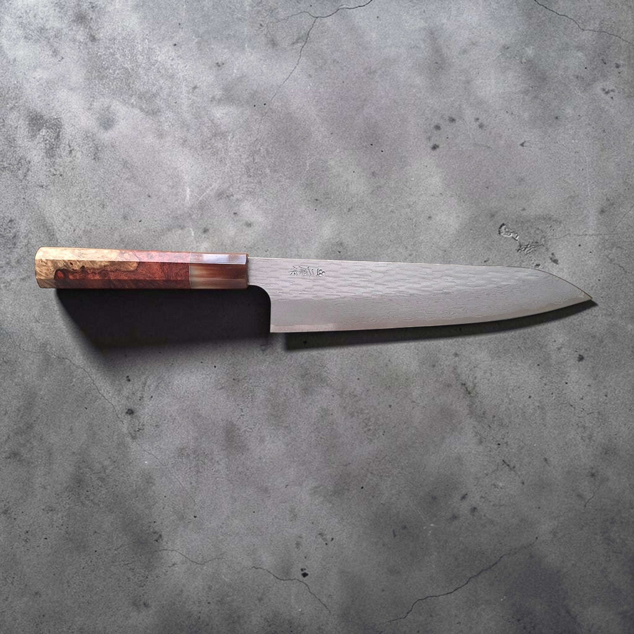 Nigara VG XEOS Tsuchime Gyuto 210 mm with amboyna burl and horn handle, full side profile product photo on a dark grey surface.