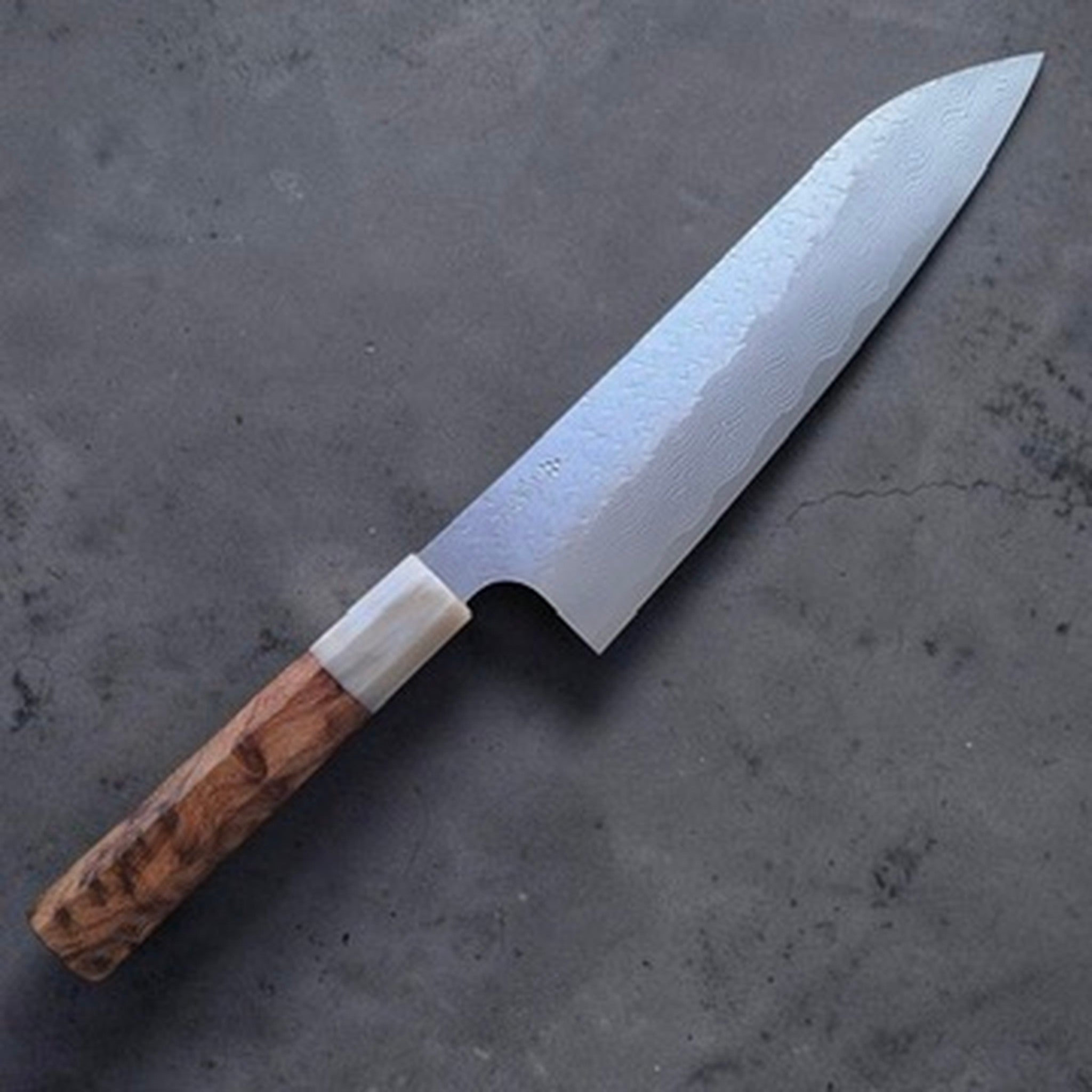 Nigara VG-XEOS Tsuchime Gyuto 210 mm with cypress and horn handle, reverse angled view on a dark grey textured surface.