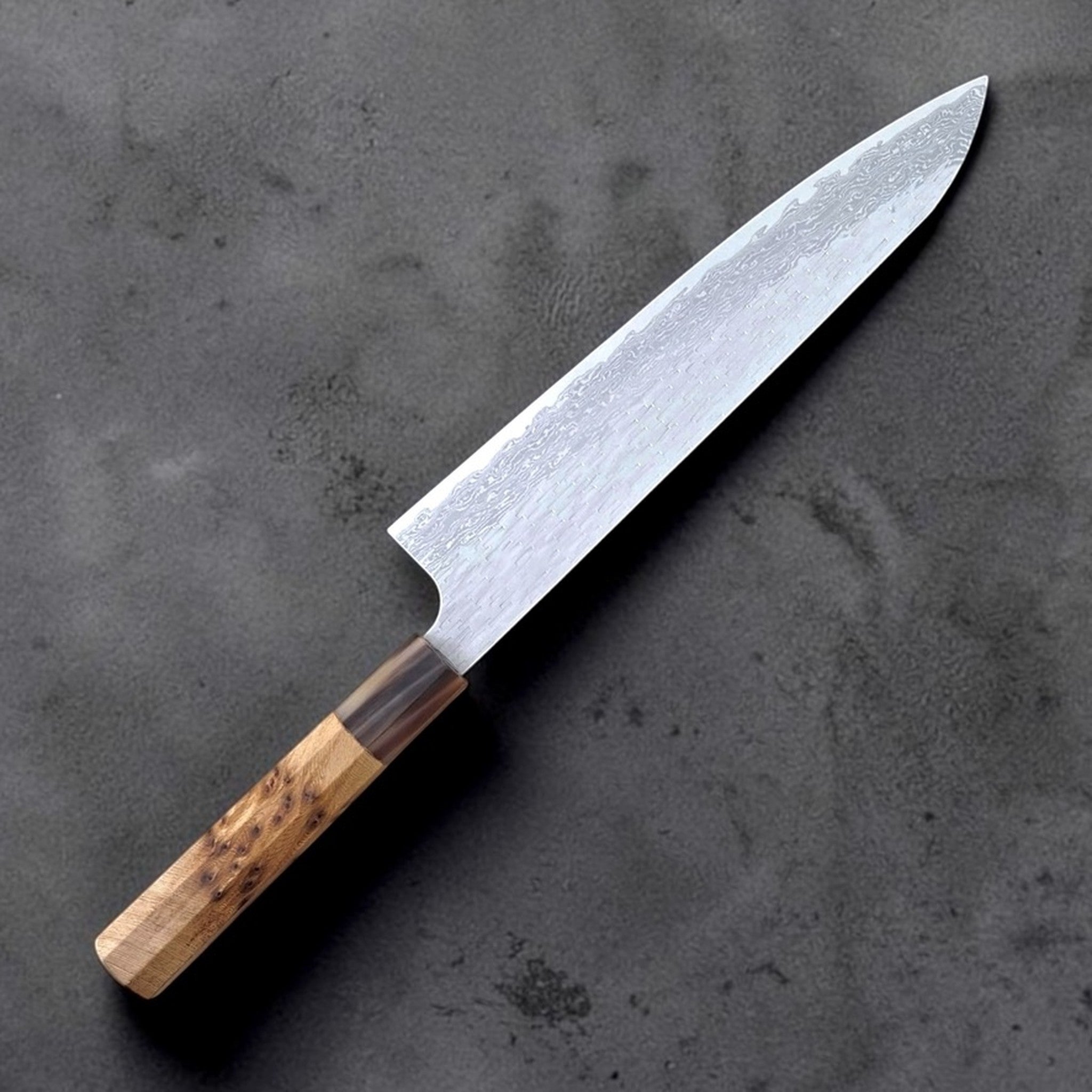 Nigara VG XEOS Tsuchime Gyuto 240 mm with cypress and horn handle, angled product photo on dark stone background.