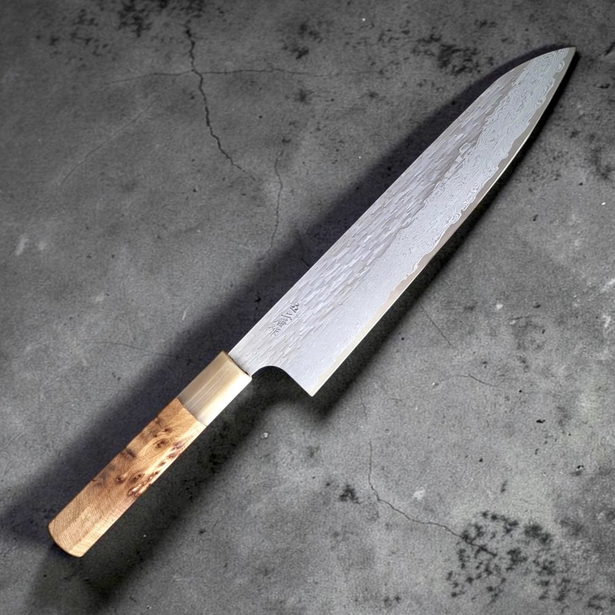 Nigara VG XEOS Tsuchime Gyuto 240 mm, angled blade photo showing tsuchime hammer marks and layered Damascus pattern.