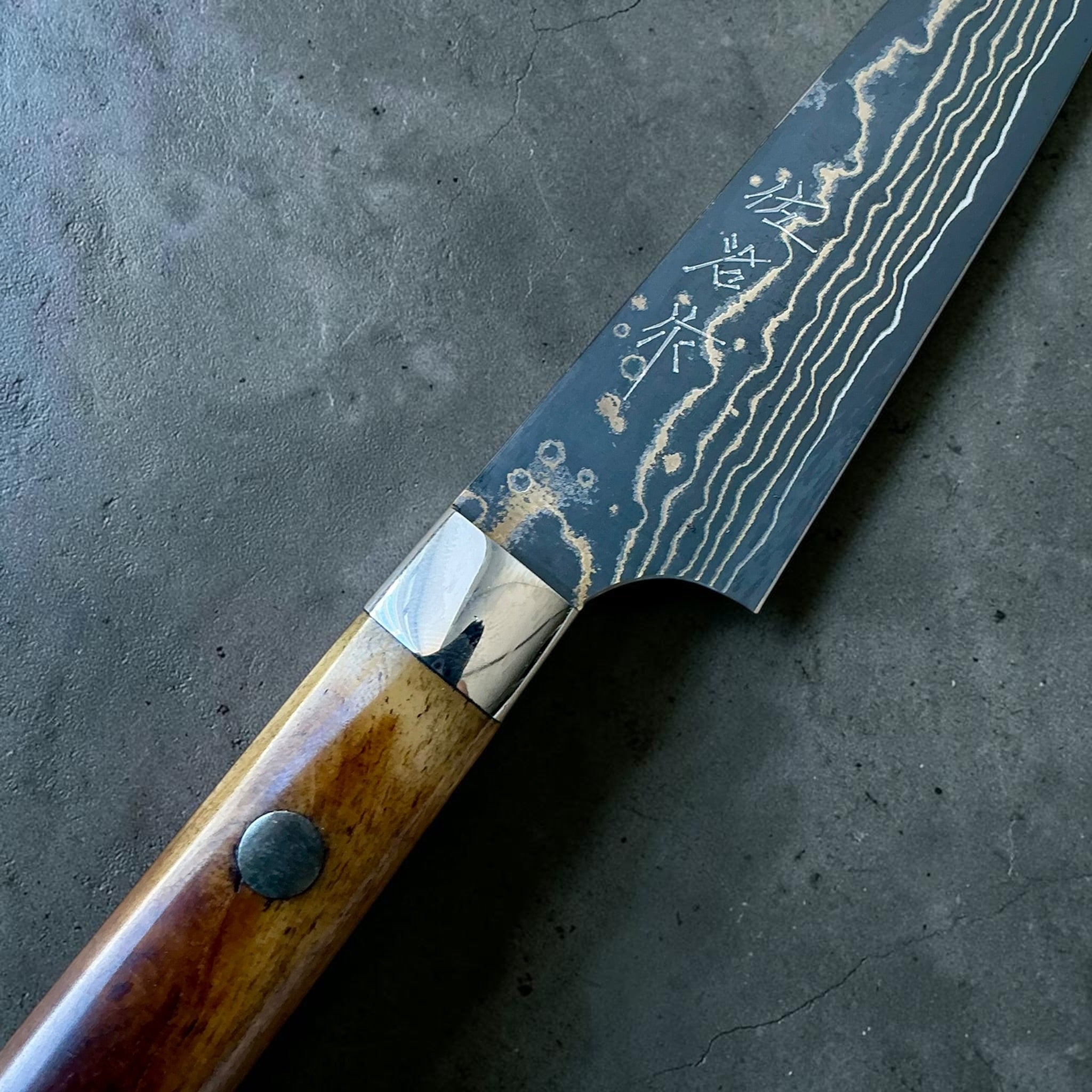 Takeshi Saji VG-10 Gold Damascus Petty 90 mm, close-up van Gold Damascus en het makersmerk.
