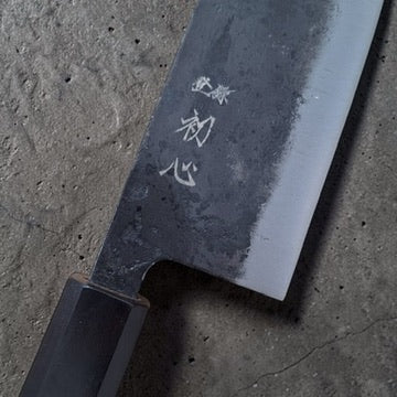 Close-up of the Hatsukokoro Kurogane santoku kanji, kurouchi finish and polished bevel