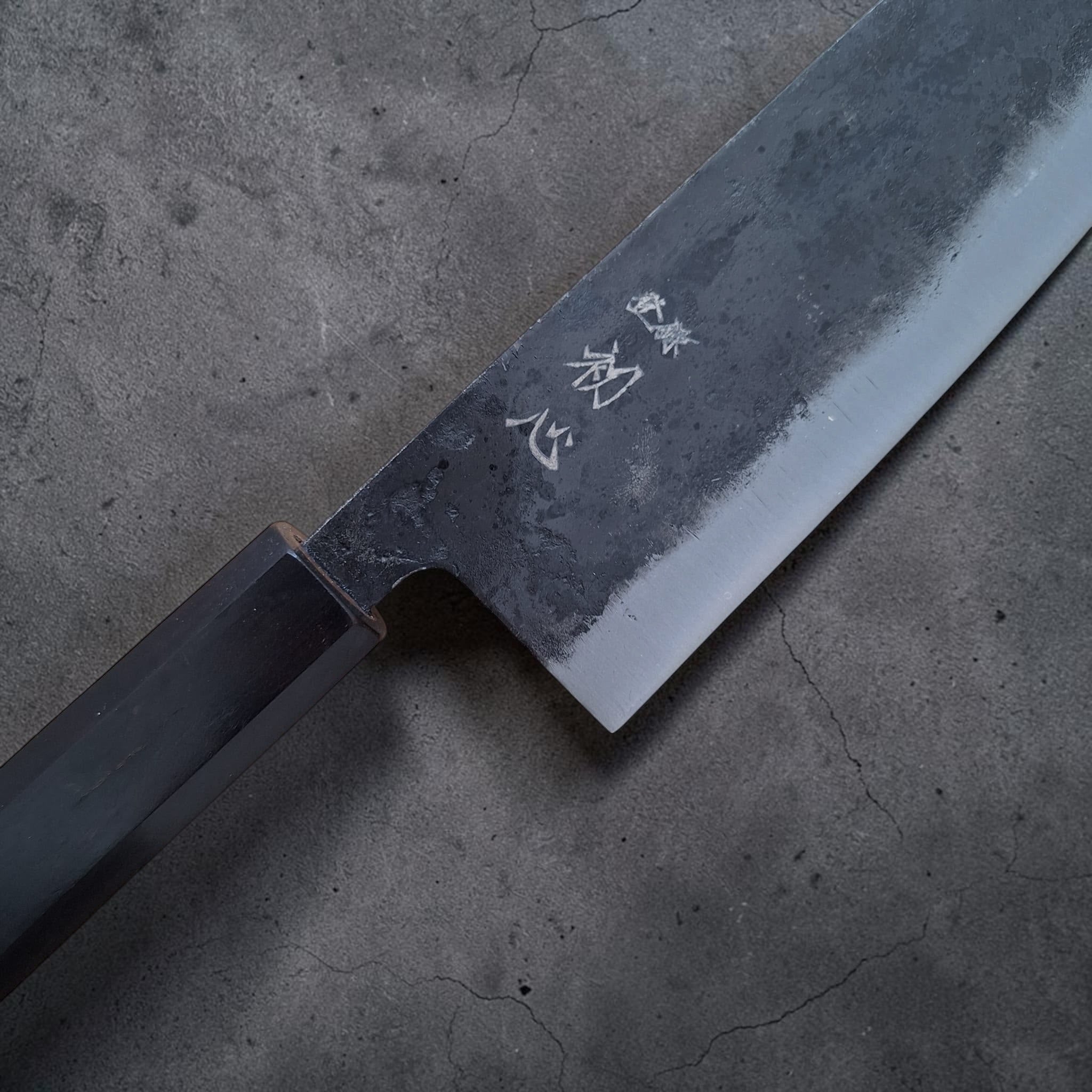 Nahaufnahme der Schmiedemarke von Hatsukokoro und der kurouchi Klinge am Kurogane Santoku