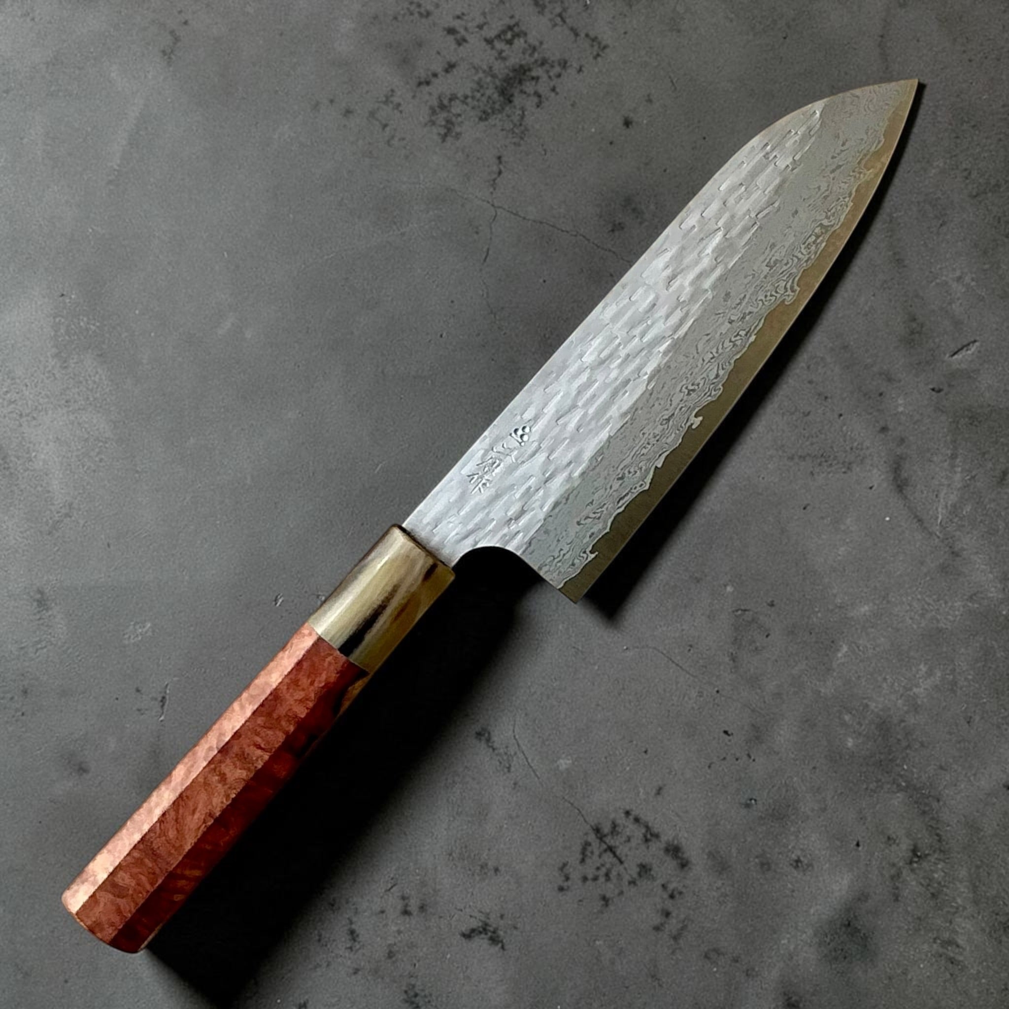 Nigara VG-XEOS polished tsuchime santoku 170mm, angled view showing hammered Damascus blade and red custom handle.
