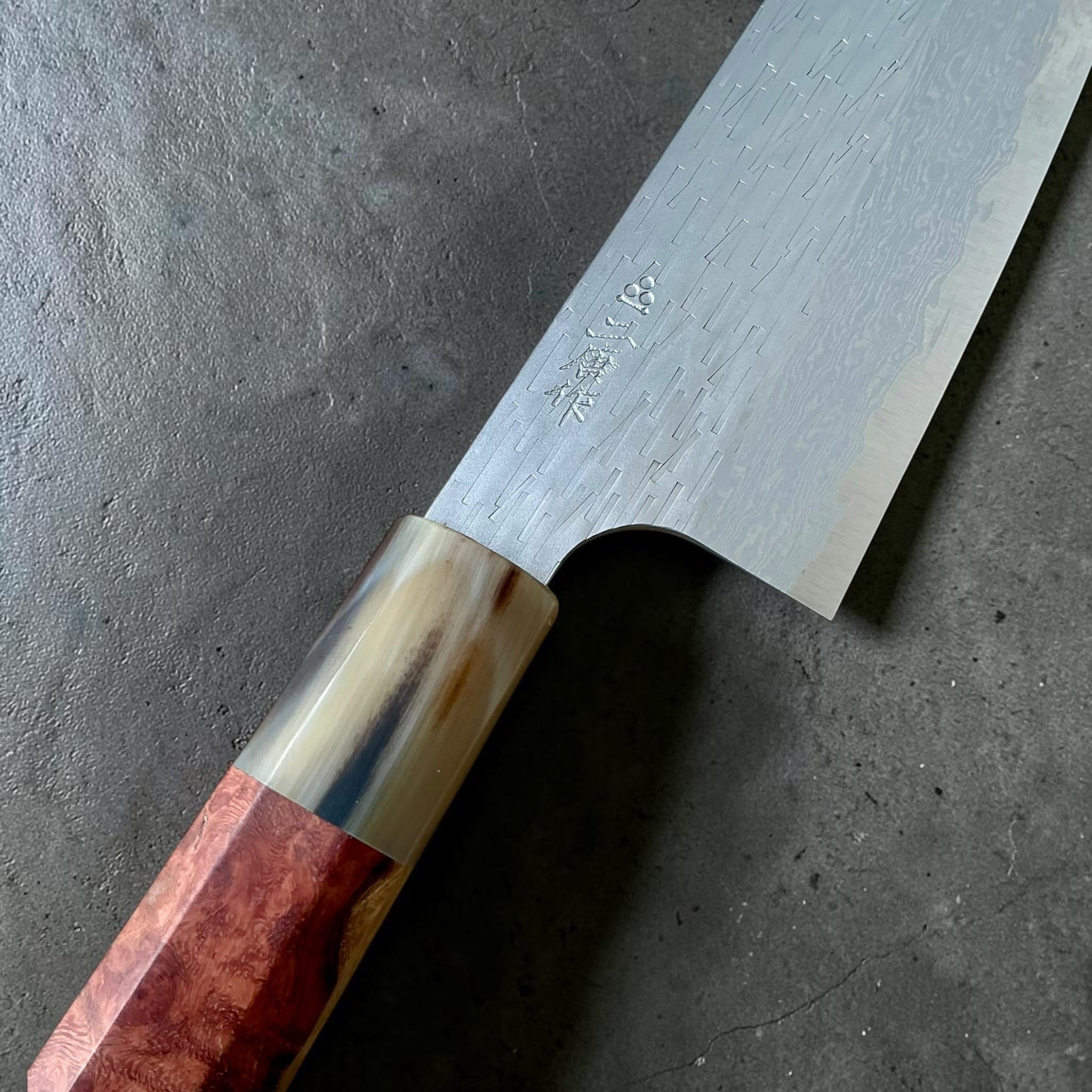 Close-up of Nigara VG-XEOS santoku showing maker's mark, polished tsuchime finish and horn ferrule.