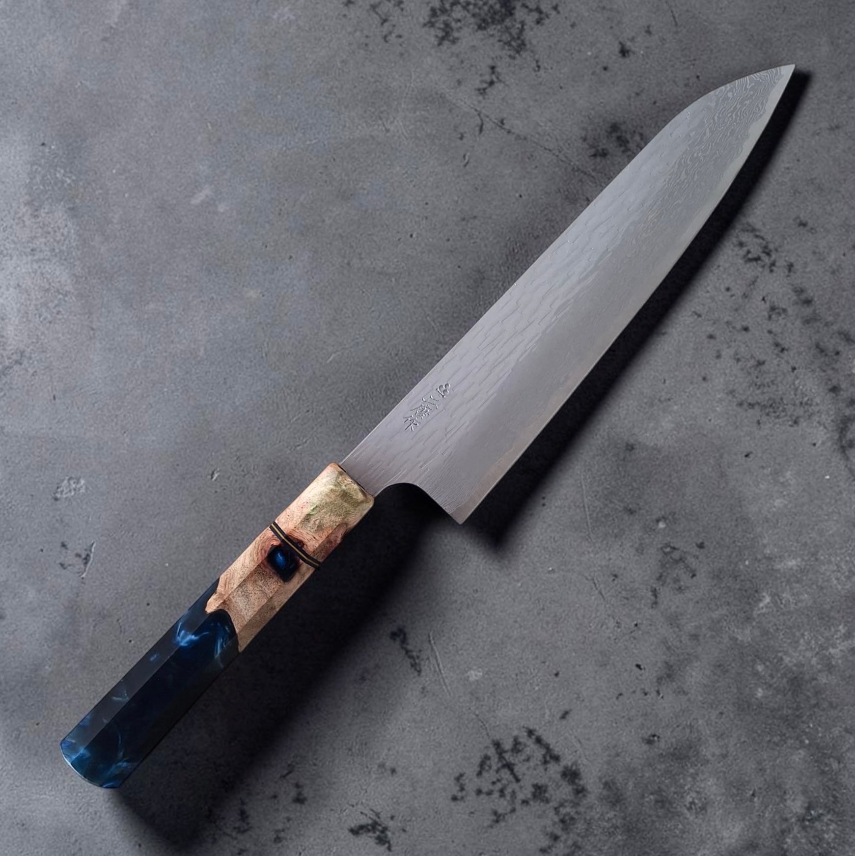 Nigara VG-XEOS Tsuchime Gyuto 210mm with blue Prisma handle, angled full-knife view showing the kanji and Damascus blade finish on a dark grey surface.