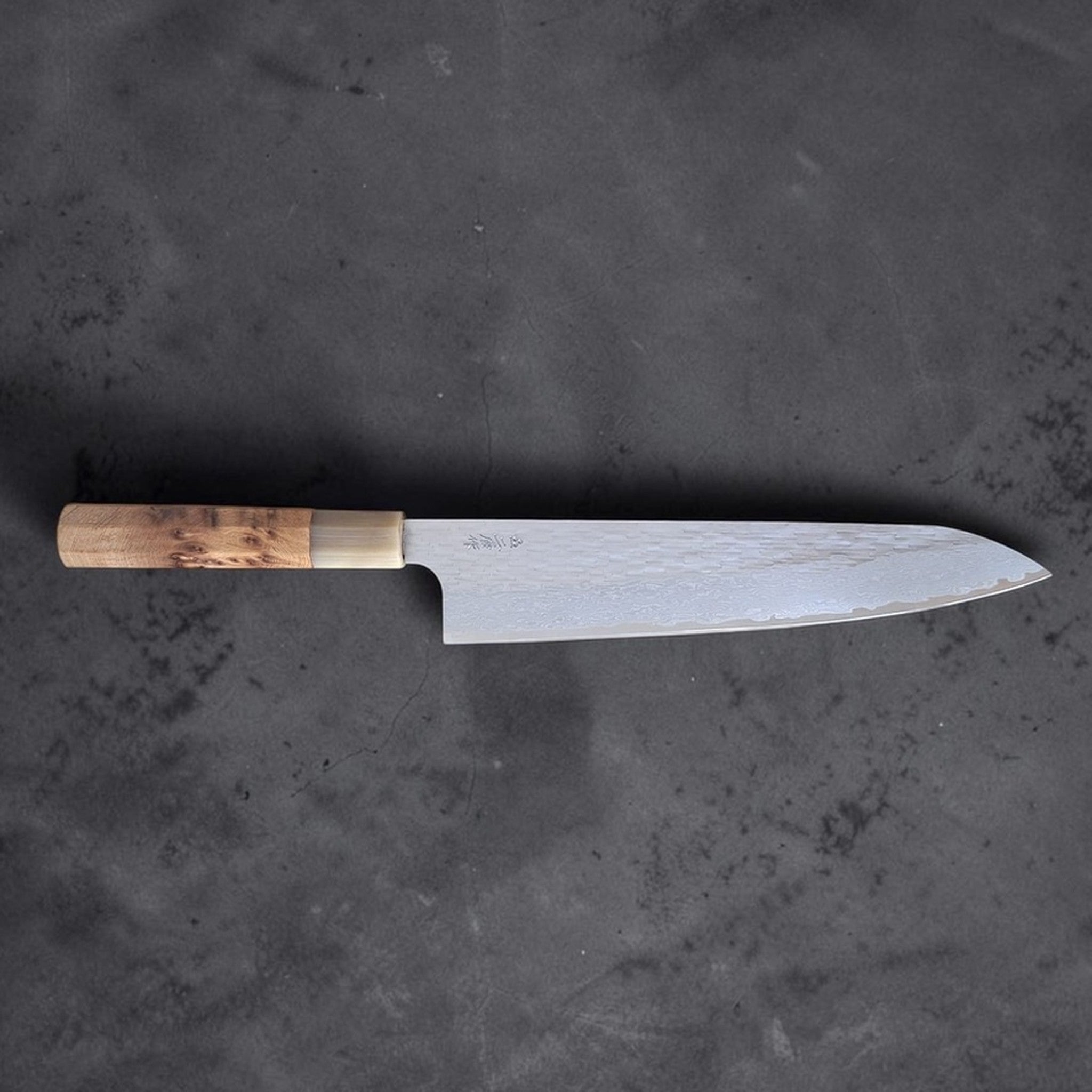 Nigara VG XEOS Tsuchime Gyuto 240 mm with cypress and horn handle, full knife profile on dark stone background.