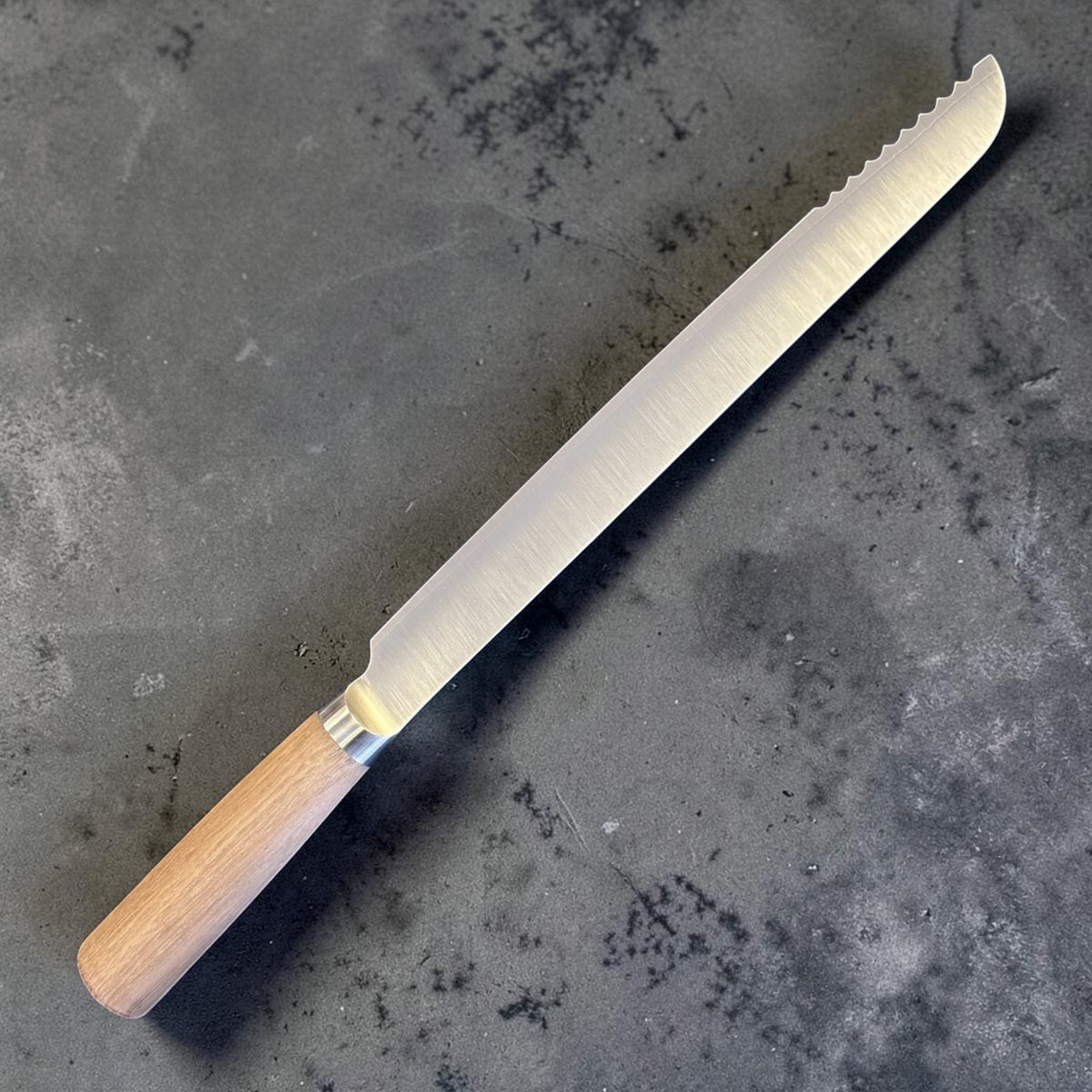 Tadafusa SLD Coltello da pane con manico in legno chiaro, vista posteriore angolata che mostra la lunga lama satinata e i denti festonati vicino alla punta.