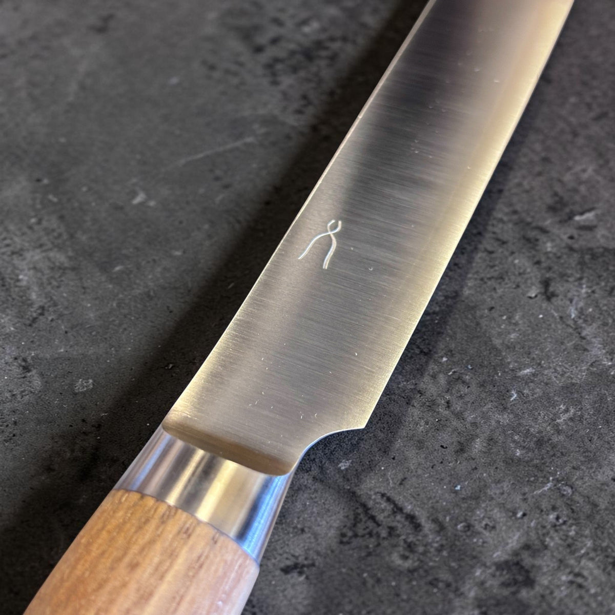 Tadafusa SLD Coltello da pane con manico in legno chiaro, primo piano della superficie della lama, del marchio del produttore e della zona del bolster.