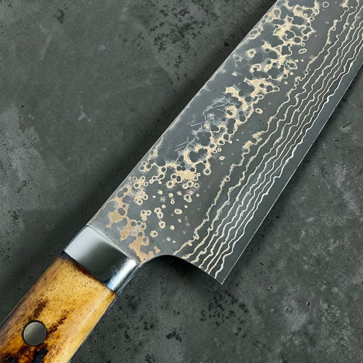 Close-up of the maker's mark and gold Damascus pattern on the Takeshi Saji Santoku