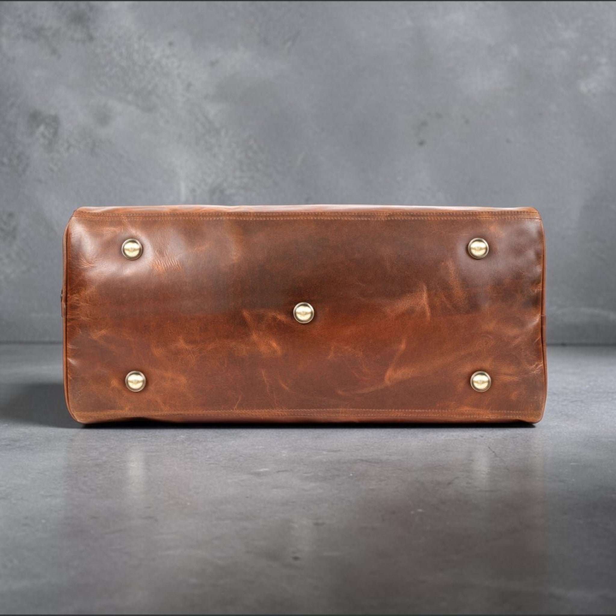 The Hidemaster Aspen Duffle Chef Bag in rustic brown leather, bottom view showing brass feet and stitched leather base.