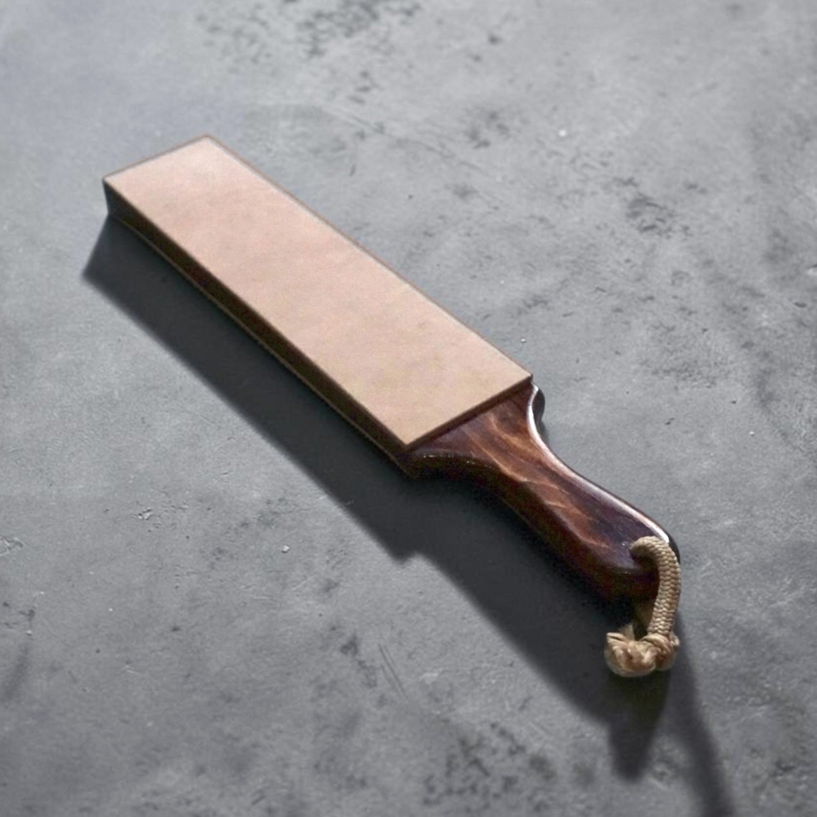 Tokushu Knife double-sided buffalo leather strop with walnut handle and vegetable-tanned leather surface shown at a three-quarter angle.