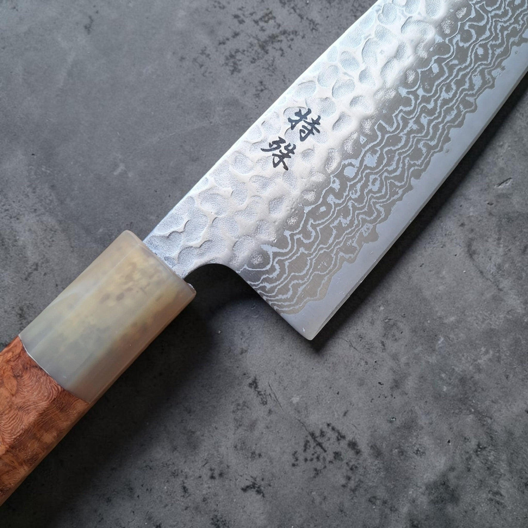 Close-up of Tokushu Knife Ginsan #3 tsuchime Damascus santoku showing etched matte finish and amboyna burl handle